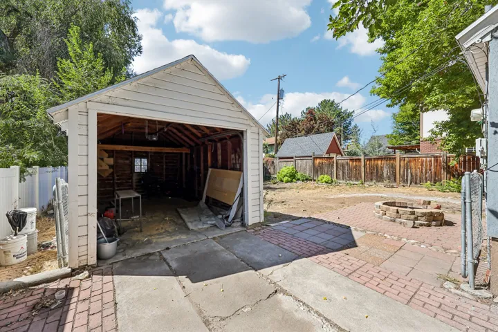 Detached garage with wood siding, concrete driveway, brick paver patio, stone fire pit, and wood fencing