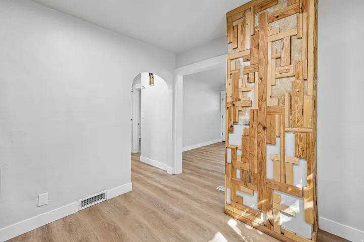 Wood-finish flooring, white walls, decorative wood-paneled accent wall, arched doorway, white trim throughout
