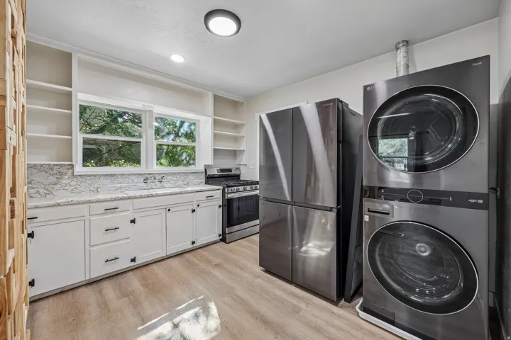 White cabinetry with dark hardware, stone-finish countertops, stainless steel appliances, wood-finish flooring, and built-in shelving