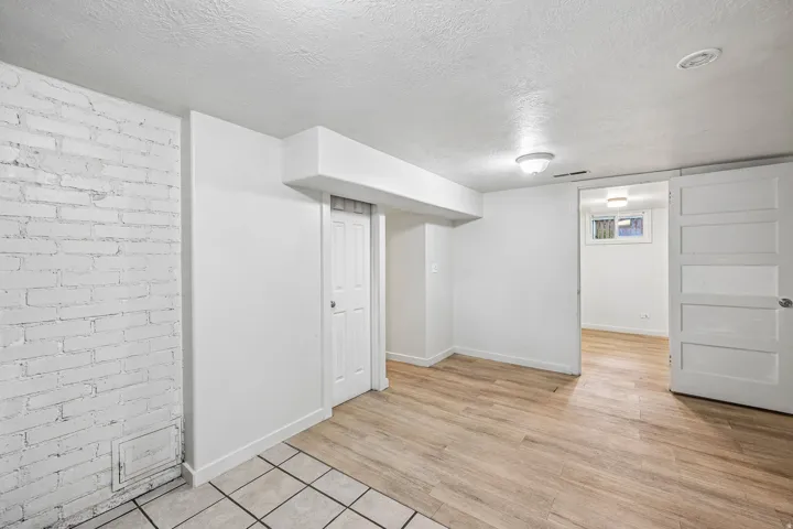 White painted brick wall, wood-finish flooring, recessed lighting, white interior doors, and a window with horizontal grilles