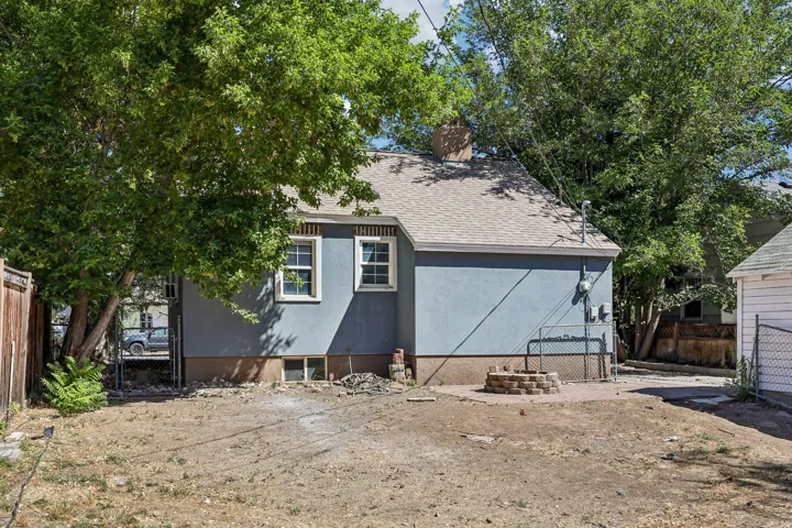 Stucco exterior featuring dual windows, a shingle roof, a brick chimney, and a built-in fire pit