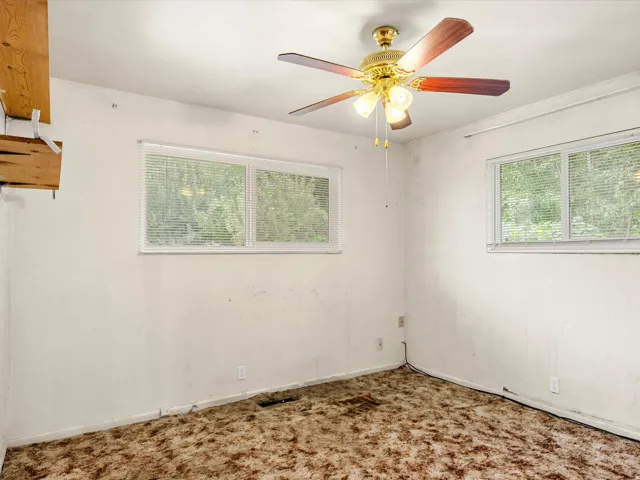 Room featuring a ceiling fan with integrated lighting, multiple windows with blinds, and built-in shelving