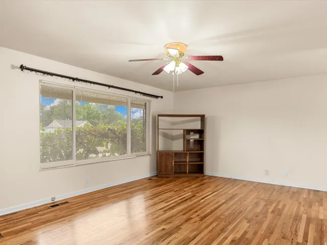 Expansive room featuring wood-finish flooring, a large window with horizontal blinds, and a ceiling fan with light fixture