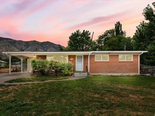 Brick exterior home with a carport, mature landscaping, and a mountain backdrop