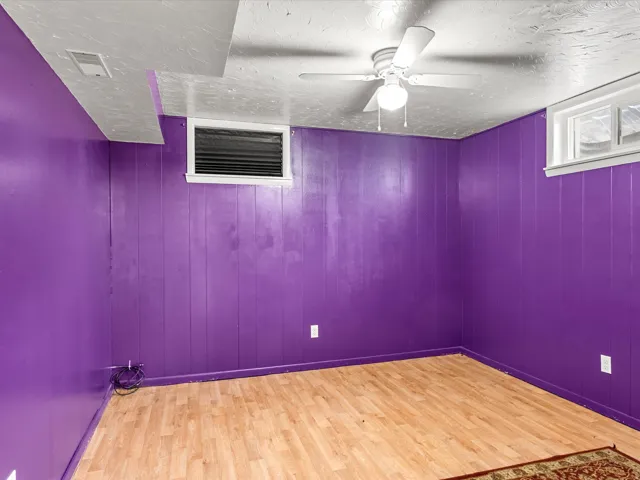 Room featuring purple paneled walls, wood-finish flooring, a ceiling fan with integrated lighting, and two windows