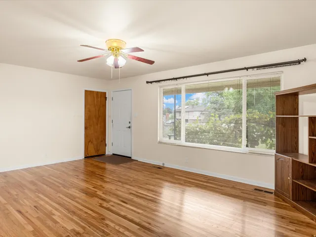 Living area featuring wood-finish flooring, a large window with blinds, and a ceiling fan with integrated lighting