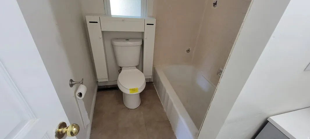 Bathroom featuring a white toilet, built-in storage, a white bathtub with tile surround, and light-toned flooring