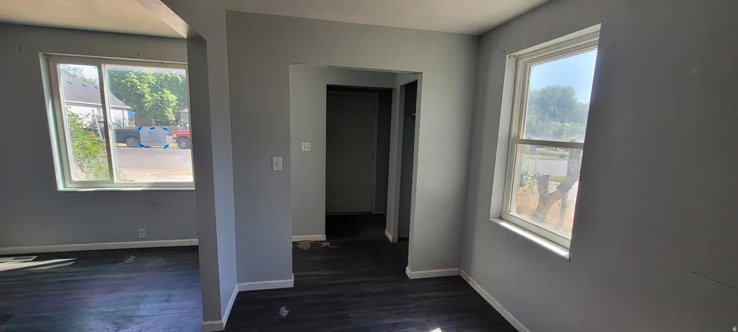 Spacious interior featuring two large windows, dark wood-finish flooring, light grey painted walls, and white baseboards