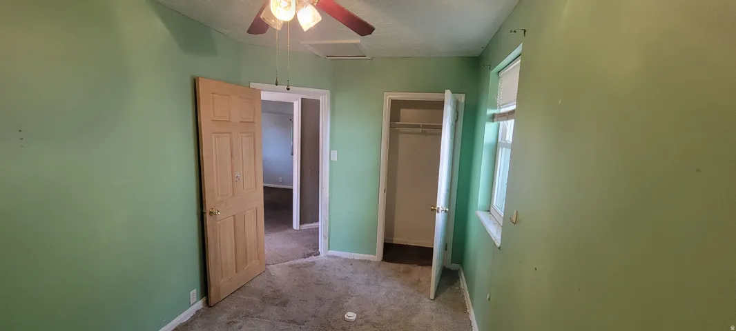 Room featuring a ceiling fan with light fixture, paneled door, window, and built-in closet