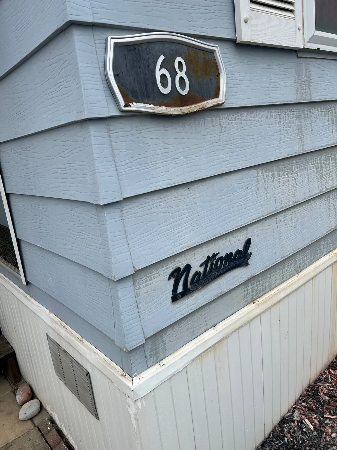 Light blue siding with textured finish, white skirting, and a black ornamental "National" plaque