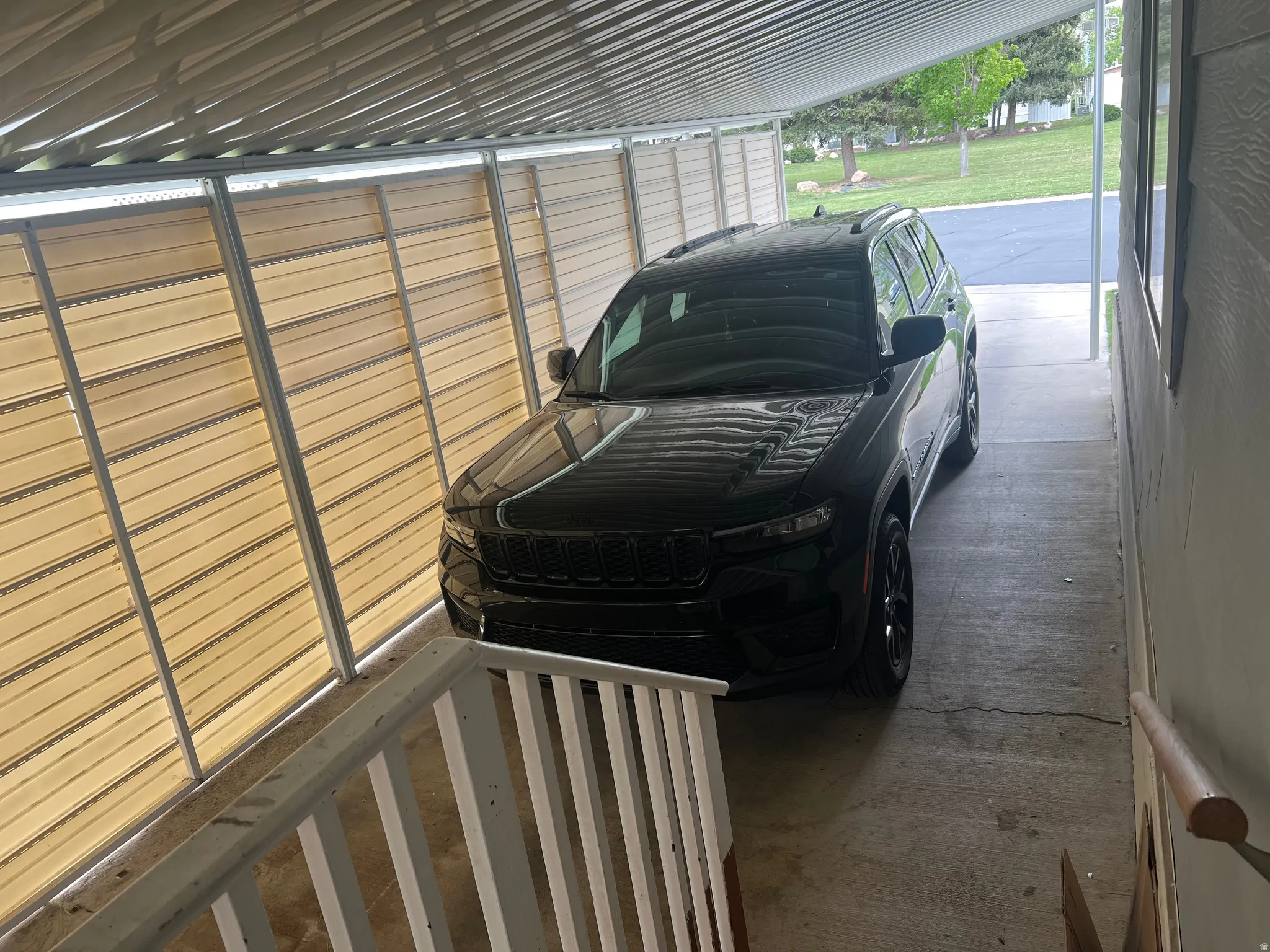 Covered carport featuring a slatted roof, privacy screening, concrete flooring, and a white railing system