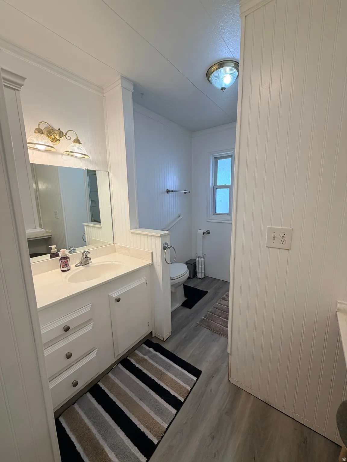 Bathroom featuring a white vanity with integrated sink, a rectangular mirror, and a brass-finish light fixture