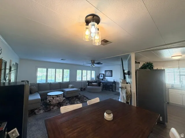 Open-concept living space featuring a dark wood-finish dining table with white chairs, a modern multi-bulb ceiling light fixture, and light-colored walls