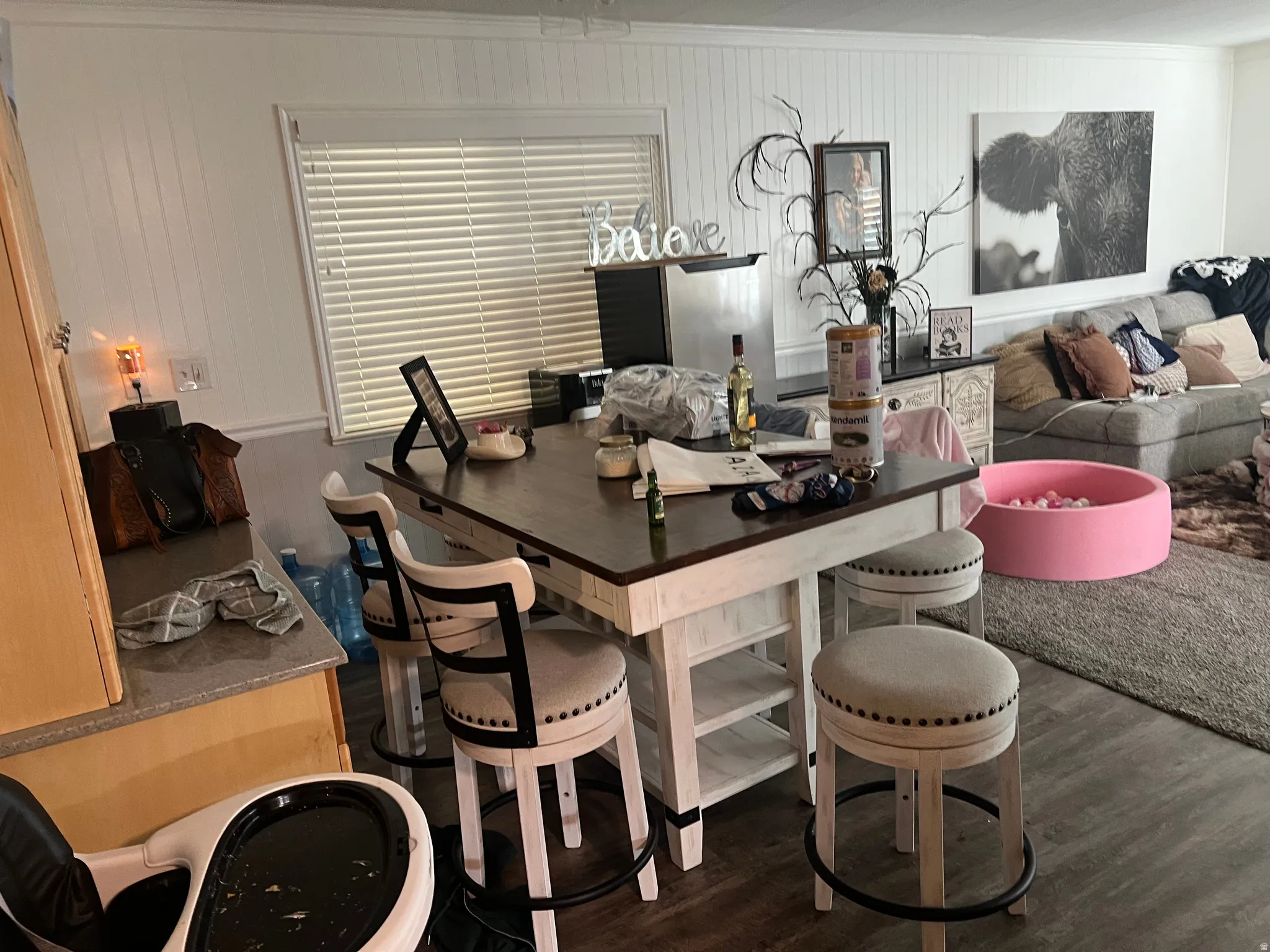Open-concept living space featuring wood-finish flooring, white shiplap wall accents, and a large window with blinds