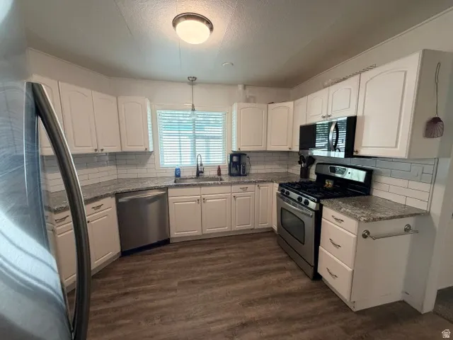 Kitchen featuring wood-finish flooring, white cabinetry, a white subway tile backsplash, light-colored speckled countertops, and stainless steel appliances
