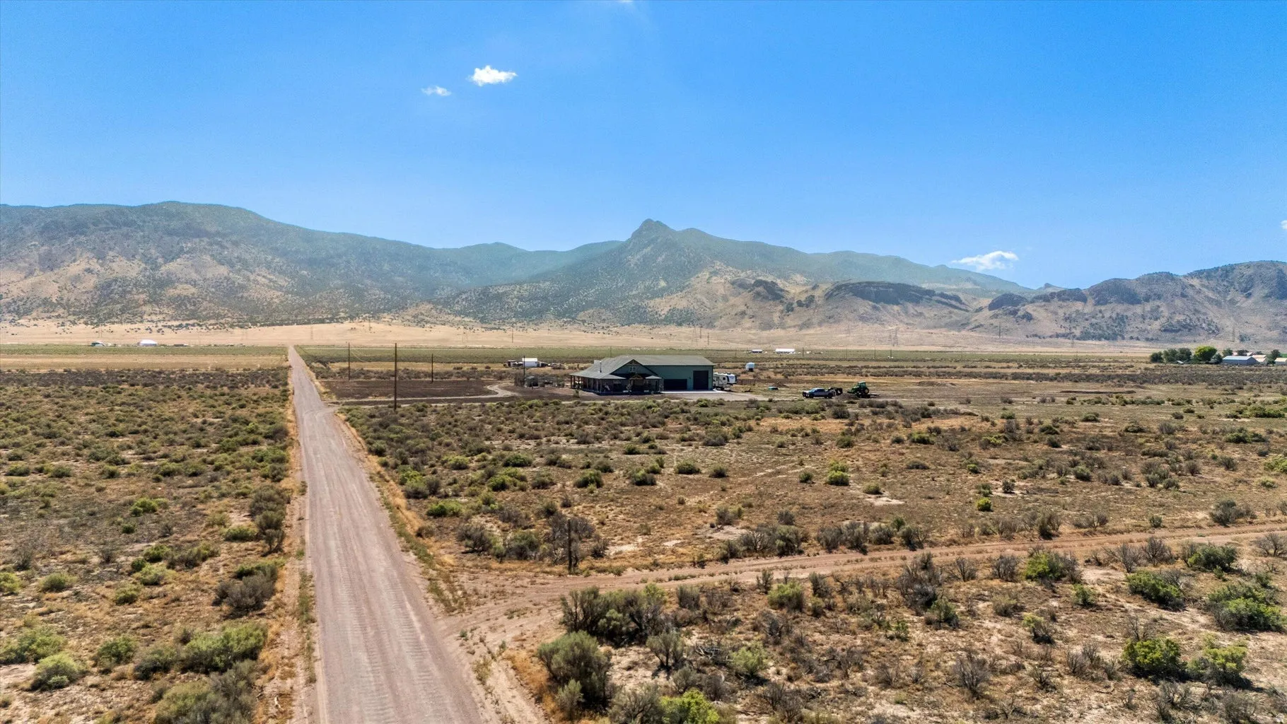 Expansive rural property featuring a long gravel driveway, mountainous backdrop, a large building with a green roof, and clear blue skies