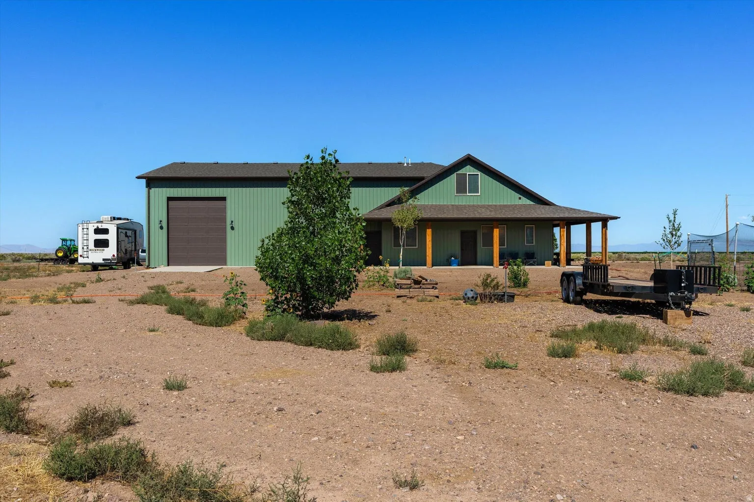 Green pole barn style residence featuring a covered porch with exposed wood columns, a prominent attached garage with a roll-up door, and a pitched roofline