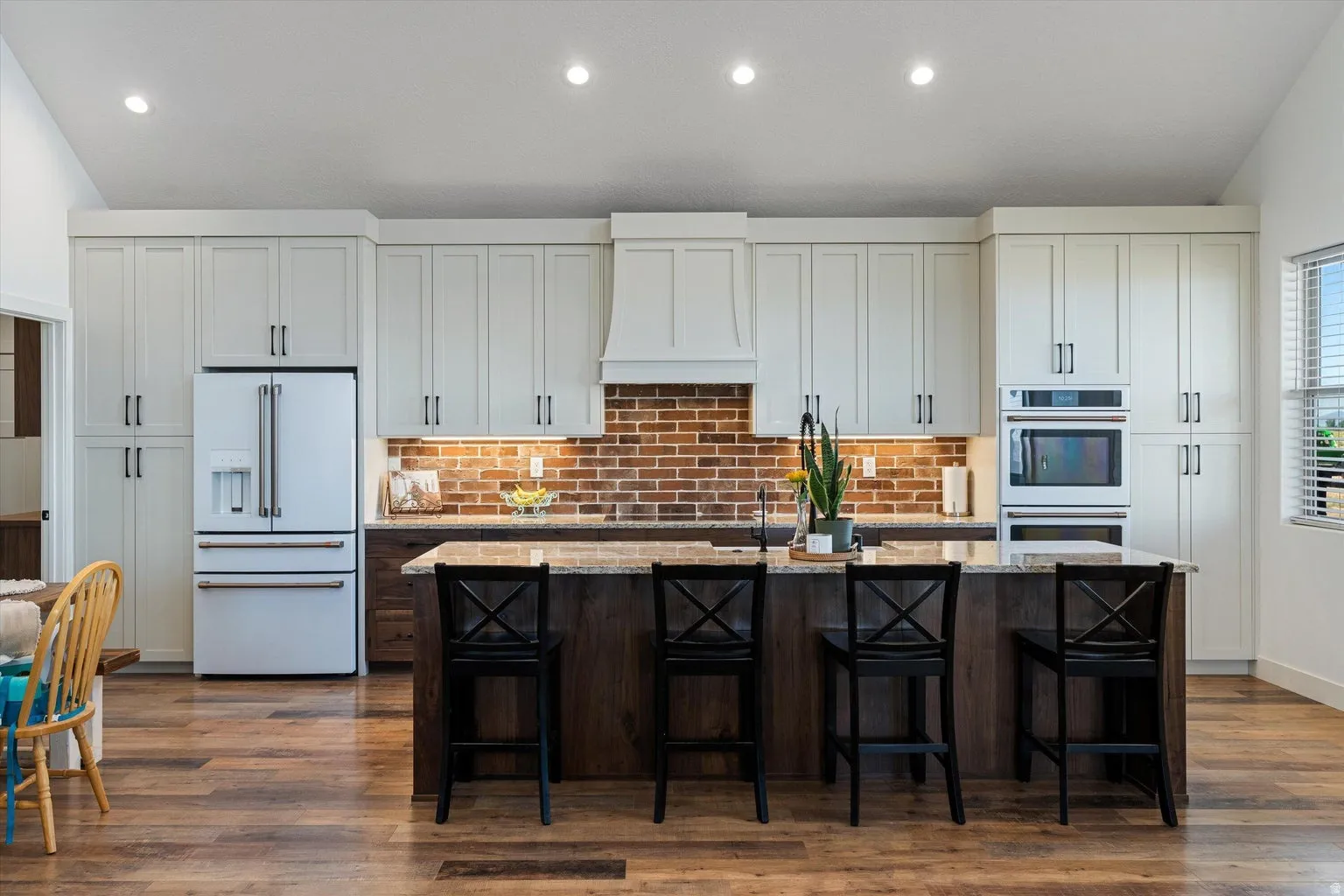 Modern kitchen featuring white shaker cabinetry, brick backsplash, wood-finish flooring, and a stone countertop island