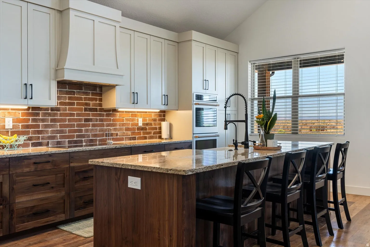 Kitchen featuring a brick-finish backsplash, two-tone cabinetry with light upper and dark lower units, granite countertops, and a center island with bar seating