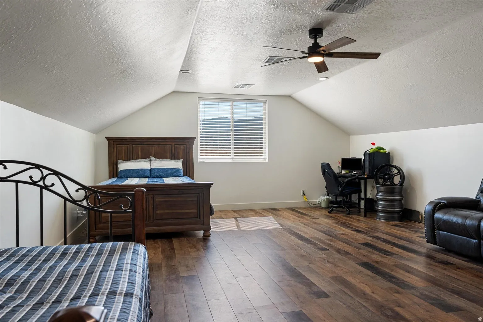 Attic space featuring wood-finish flooring, a window with horizontal blinds, sloped ceilings, and a ceiling fan with integrated lighting