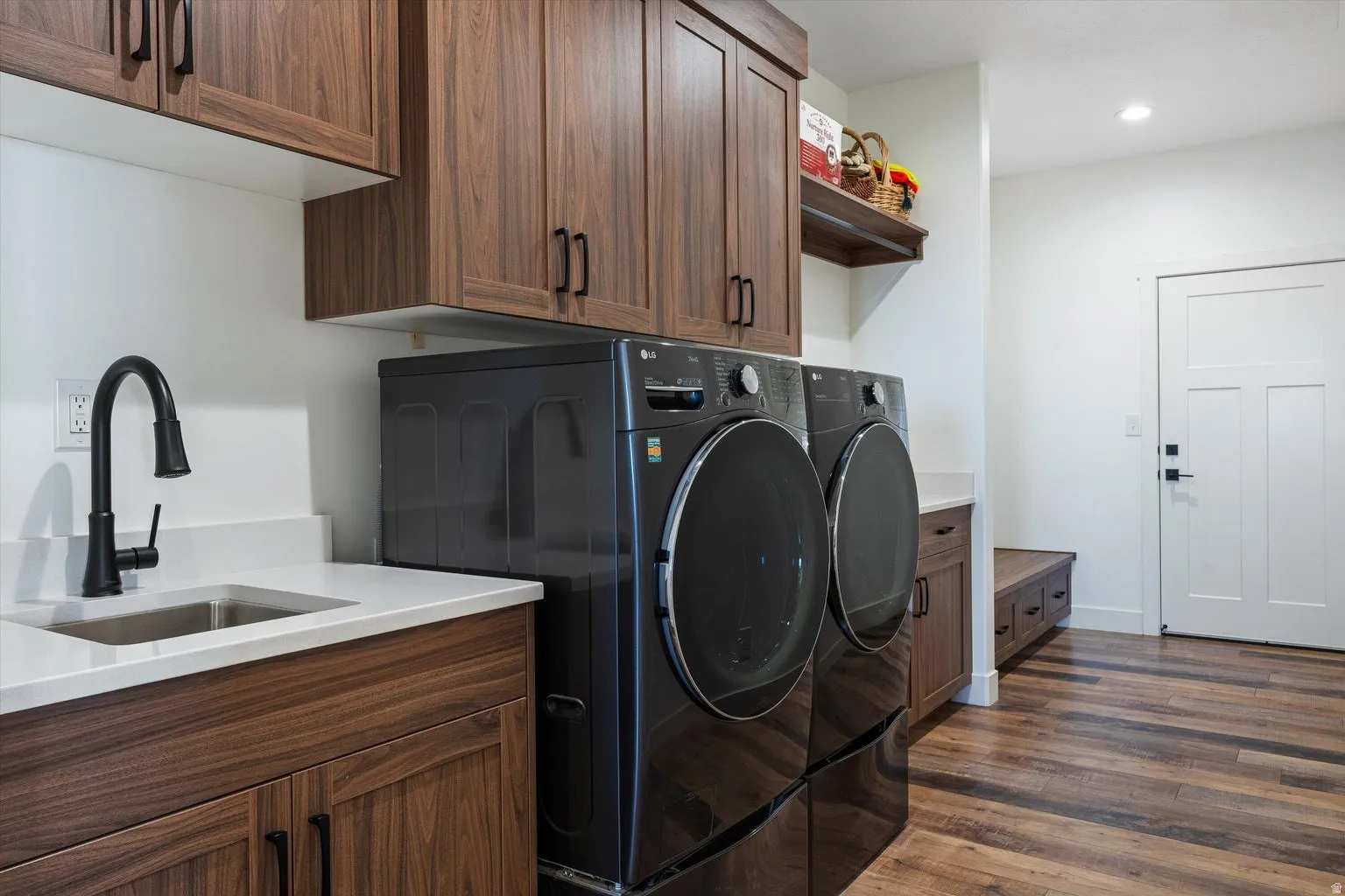 Laundry area featuring wood-finish cabinetry, a white countertop with an undermount sink, and a matte black faucet