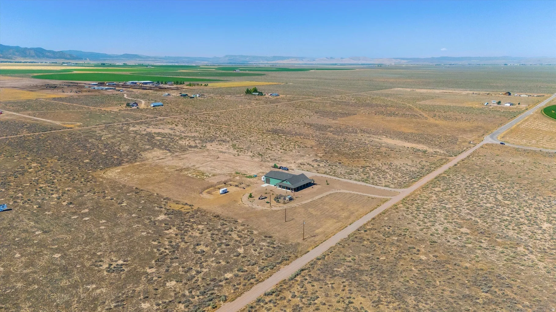 Expansive property featuring a single-story residence with a dark roofline, surrounded by arid landscape