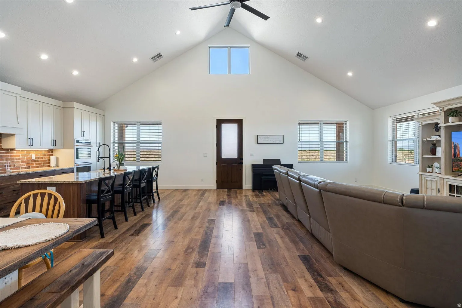 Open concept living area featuring wood-finish flooring, a vaulted ceiling with a ceiling fan, and recessed lighting