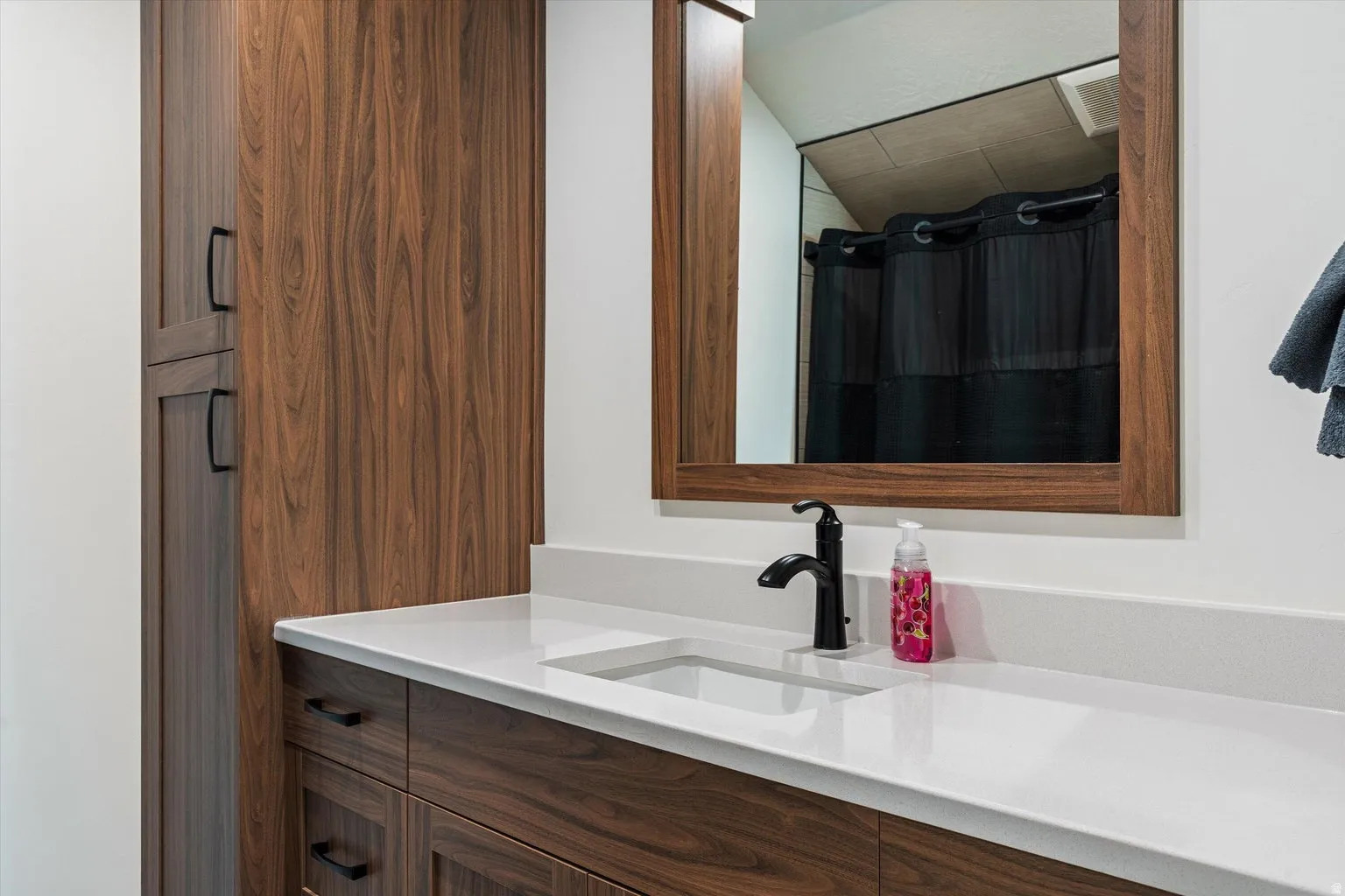 Bathroom vanity featuring a light-toned countertop with an integrated rectangular sink, matte black faucet, and wood-finish cabinetry