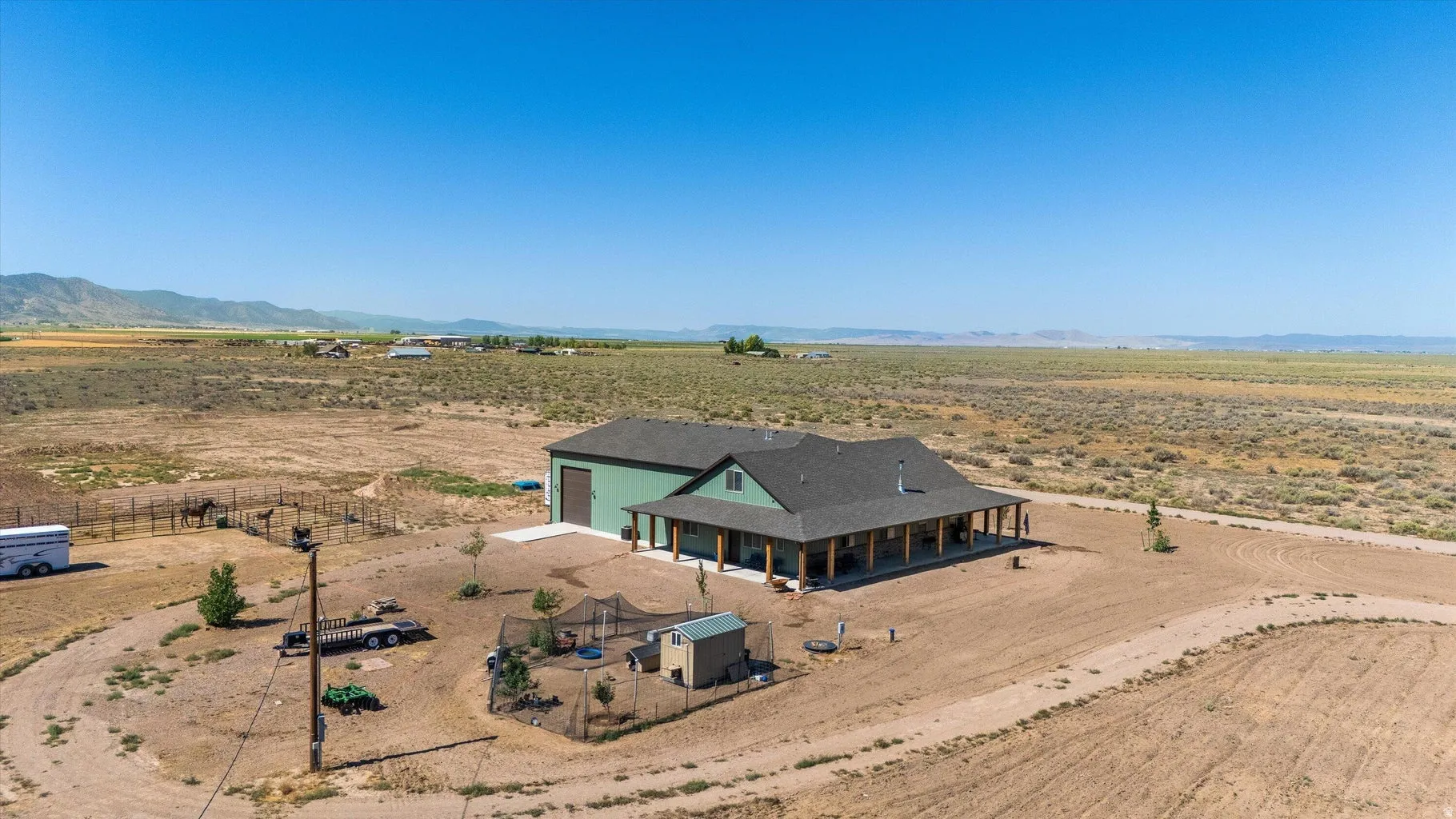Expansive desert property featuring a single-story residence with a wraparound covered porch, a large detached garage, and a fenced animal enclosure