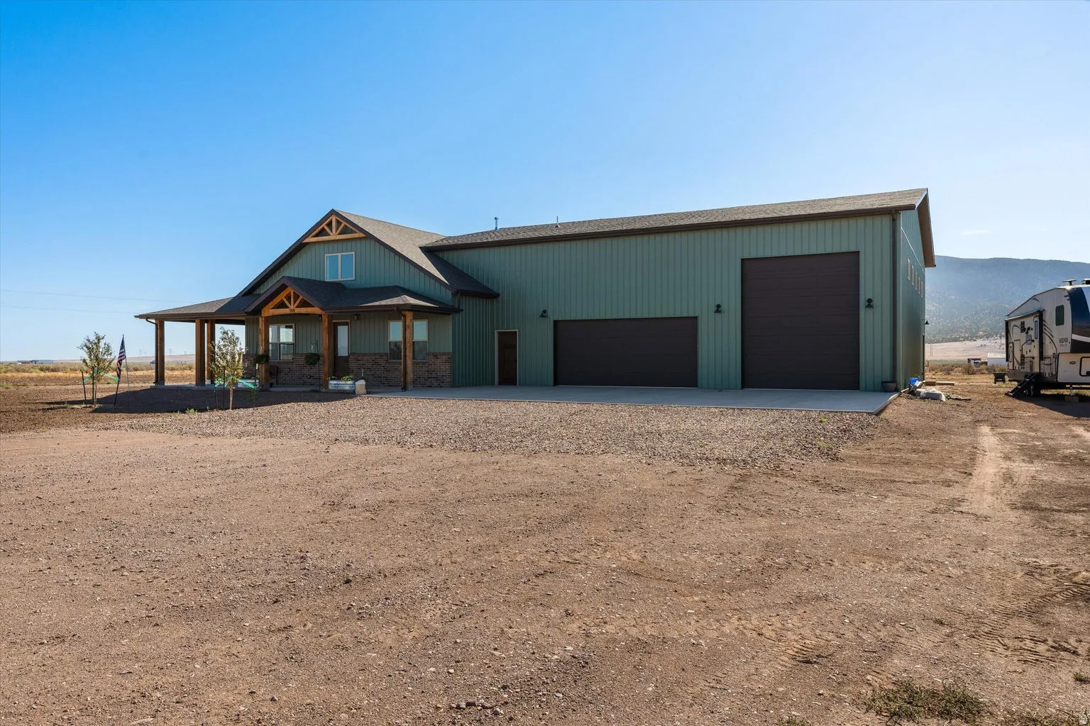 Modern barn-style home featuring a covered front porch, stone accents, two large garage doors, and a gravel driveway