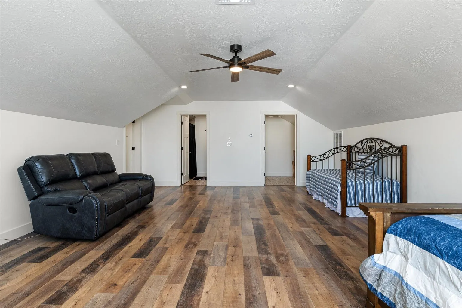 Spacious room featuring wood-finish flooring, a sloped ceiling, and a ceiling fan with integrated lighting