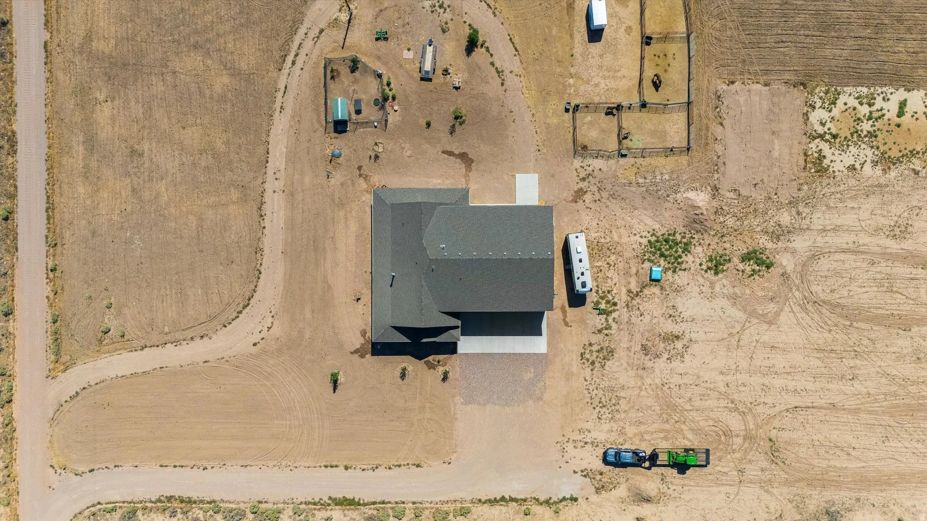 Aerial property view featuring a dark shingled roof, concrete driveway, and surrounding open land
