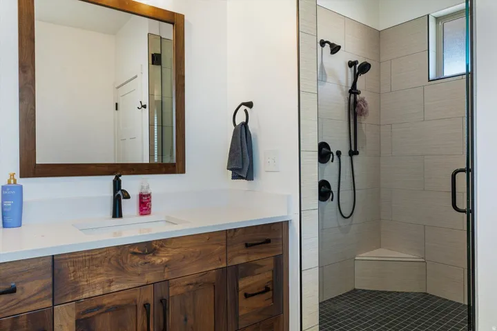 Walk-in shower with light-toned rectangular tile surround, black grid-patterned floor tile, and a built-in corner bench