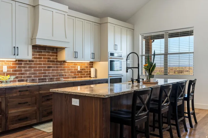 Kitchen featuring a brick-finish backsplash, two-tone cabinetry with light upper and dark lower units, granite countertops, and a center island with bar seating