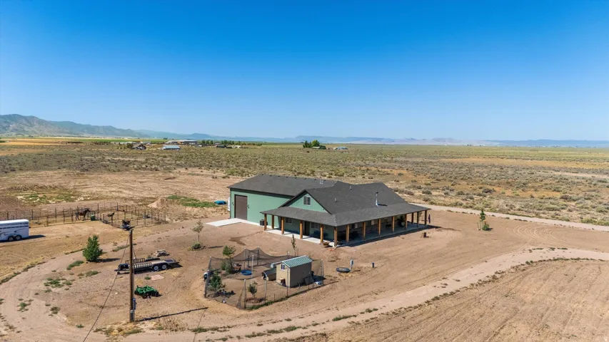 Expansive desert property featuring a single-story residence with a wraparound covered porch, a large detached garage, and a fenced animal enclosure