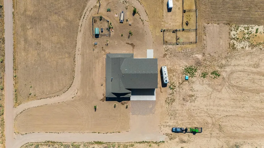 Aerial property view featuring a dark shingled roof, concrete driveway, and surrounding open land