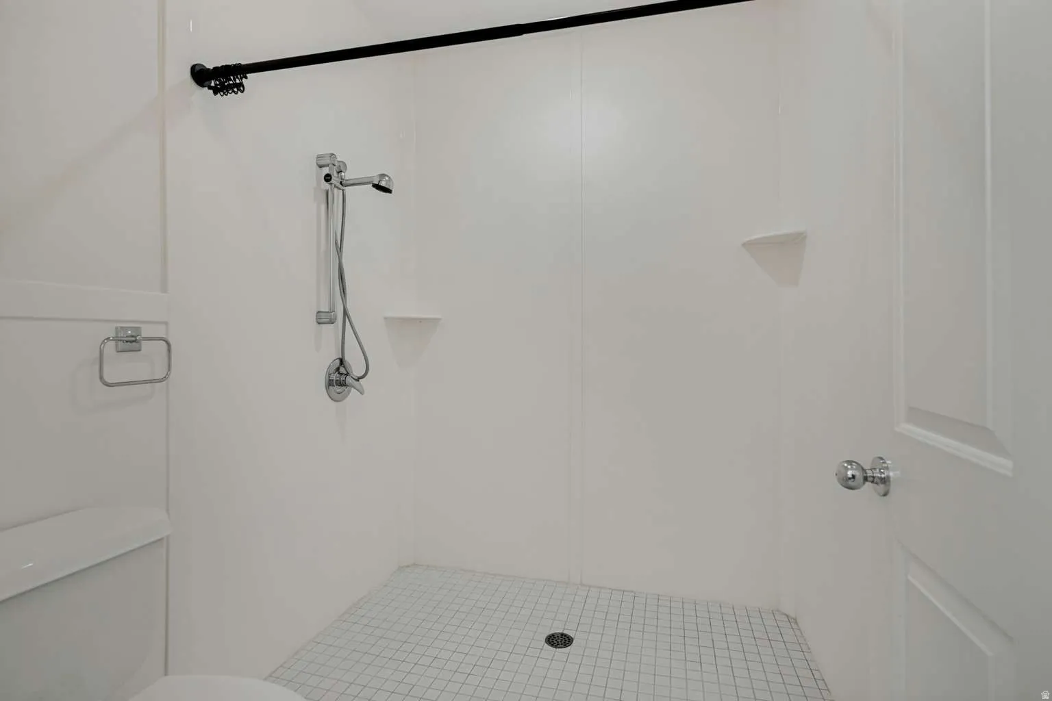Shower with white panel walls, chrome fixtures, and white mosaic tile flooring