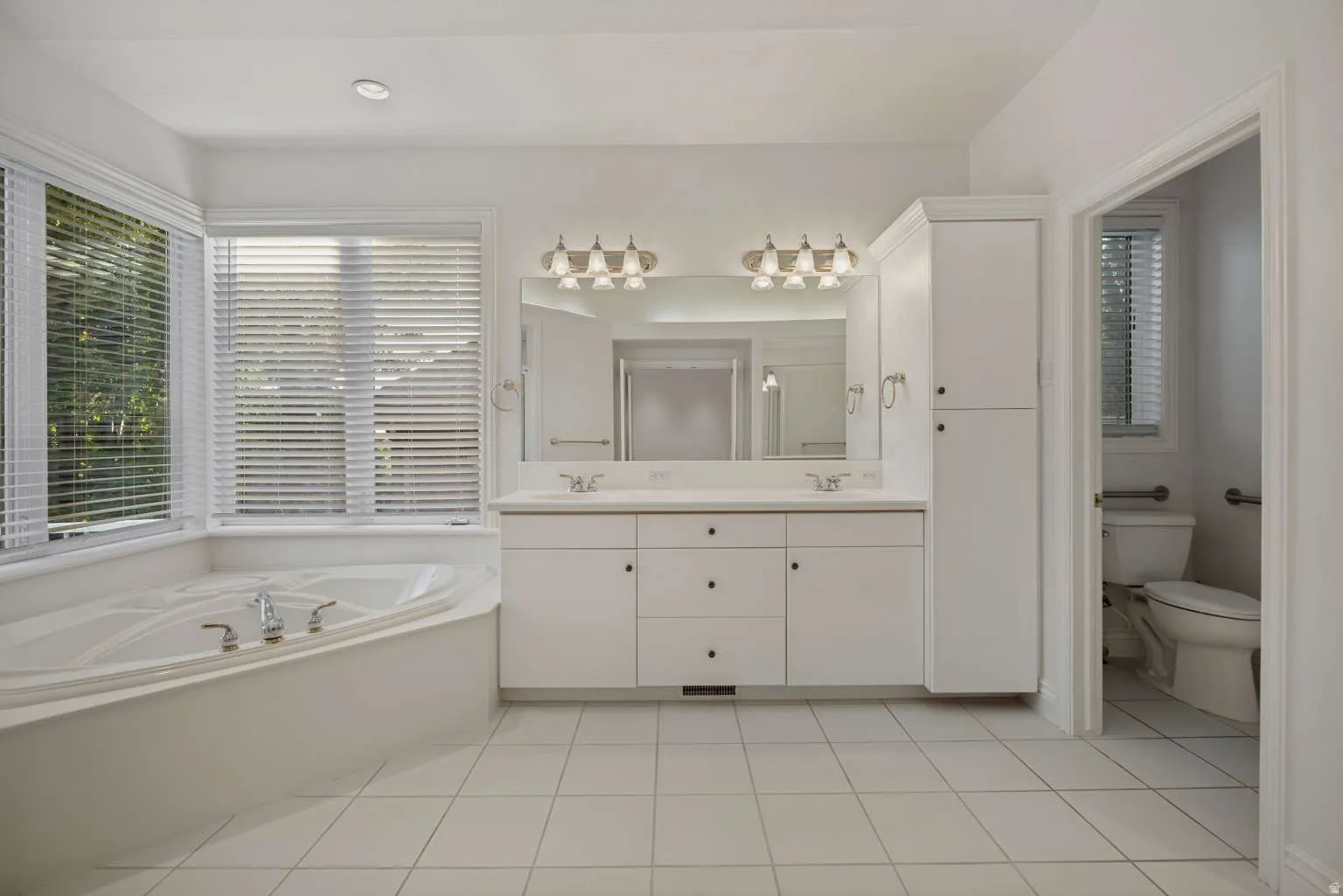 Recessed lighting, tile flooring, dual vanity with a large mirror, built-in soaking tub, and a tall built-in storage cabinet