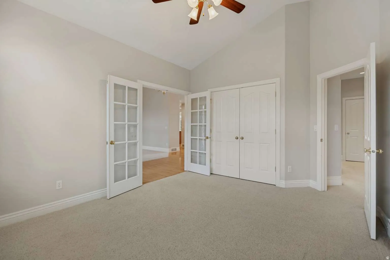 Vaulted ceiling with ceiling fan, light neutral-toned carpeting, double French doors, double panel closet doors, and light wall paint
