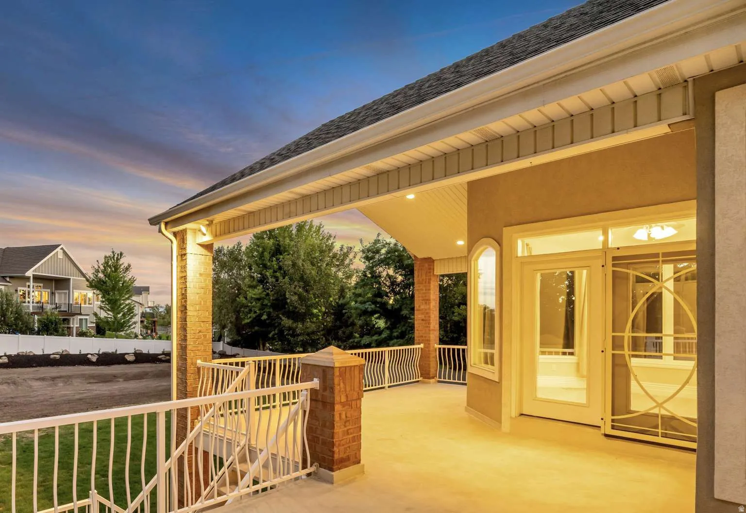 Expansive covered patio with recessed lighting, brick pillars, white railing, and exterior stucco finish