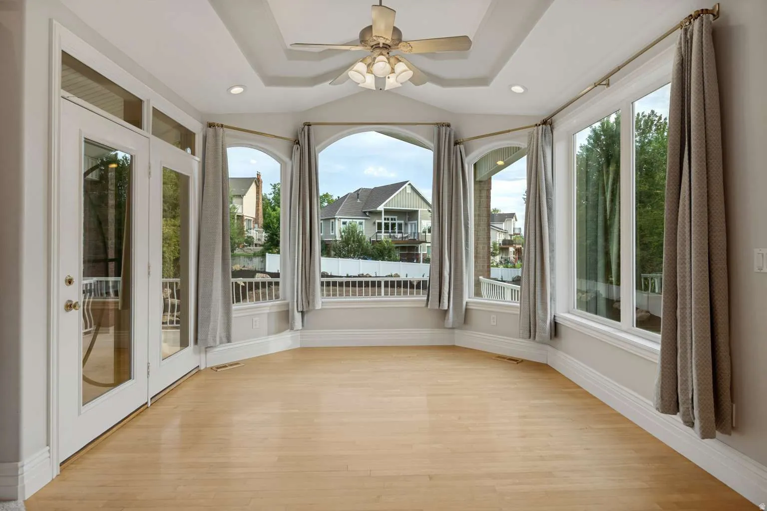 Bright room with wood-finish flooring, a tray ceiling, and a ceiling fan