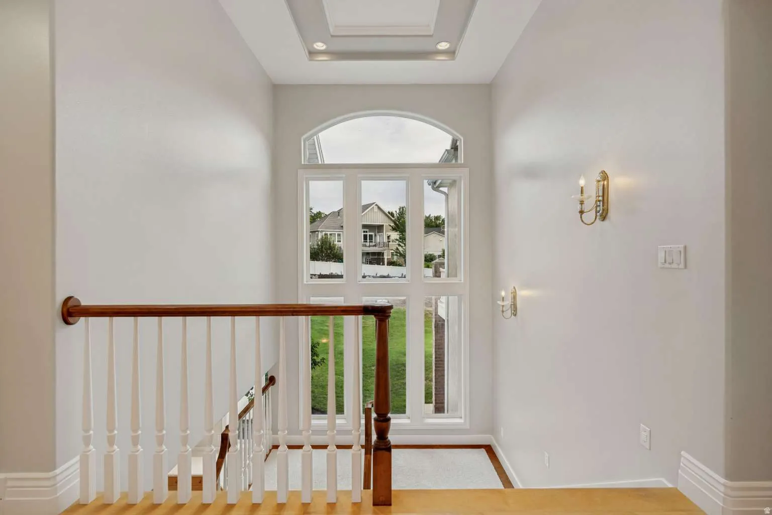 Arched window with multiple panes, recessed ceiling lighting, decorative wall sconces, wood-finish flooring, and a classic wood and white baluster staircase