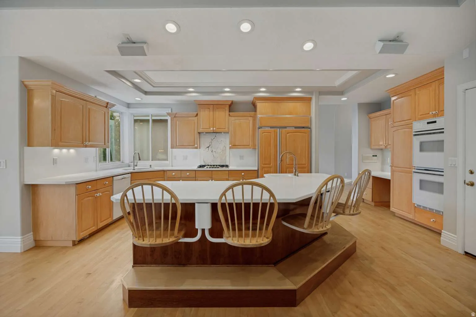Spacious kitchen featuring light wood cabinetry, white countertops, built-in double ovens, a center island with seating, and recessed lighting