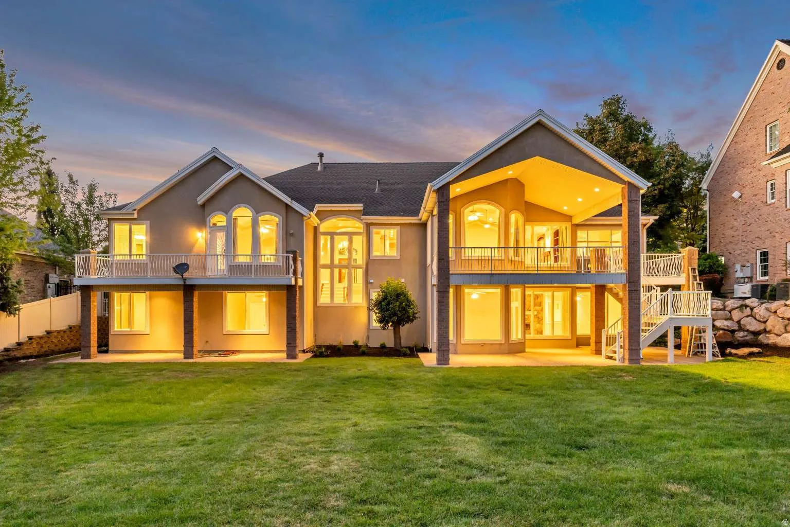 Expansive rear exterior featuring a covered patio, multiple upper-level balconies, architectural windows, and a manicured lawn