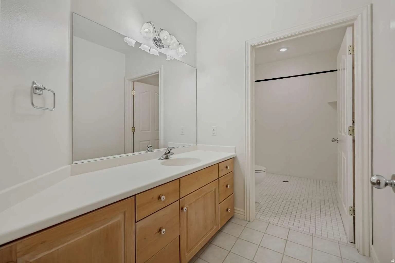Wide vanity with a light-toned countertop, wood-finish cabinetry, and a large wall-mounted mirror