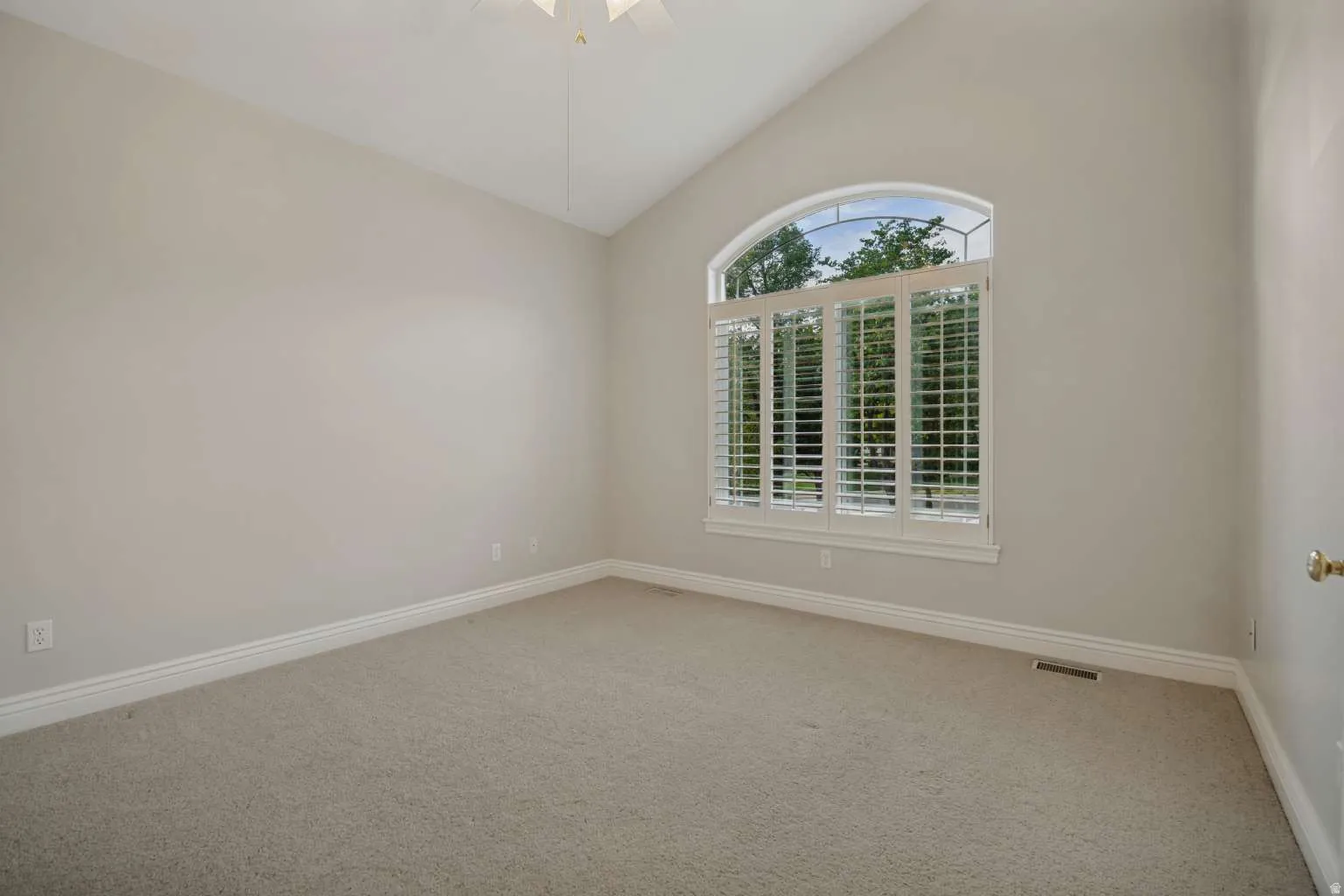 Vaulted ceiling with a ceiling fan, arched window with plantation shutters, and neutral carpeting