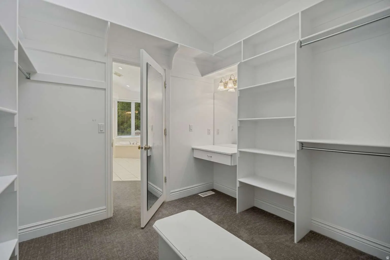 Built-in shelving, vanity desk with built-in drawer, garment rods, wall-mounted light fixture, and carpet flooring