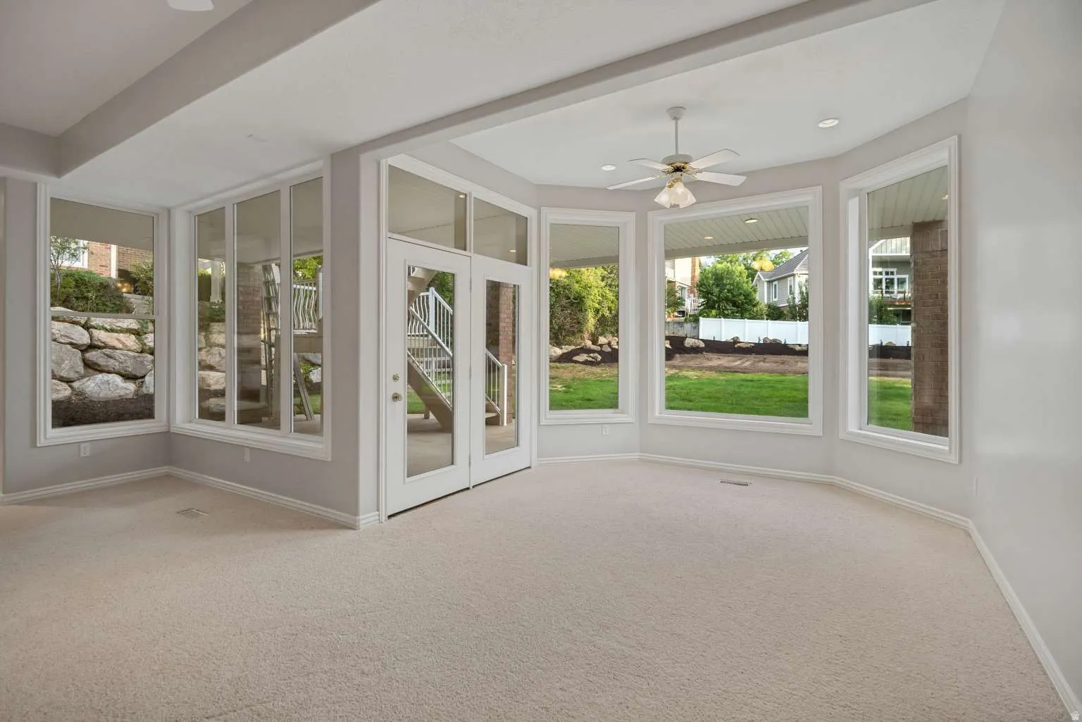 Wall-to-wall carpeting, extensive window placement, recessed lighting, ceiling fan, and double glass doors