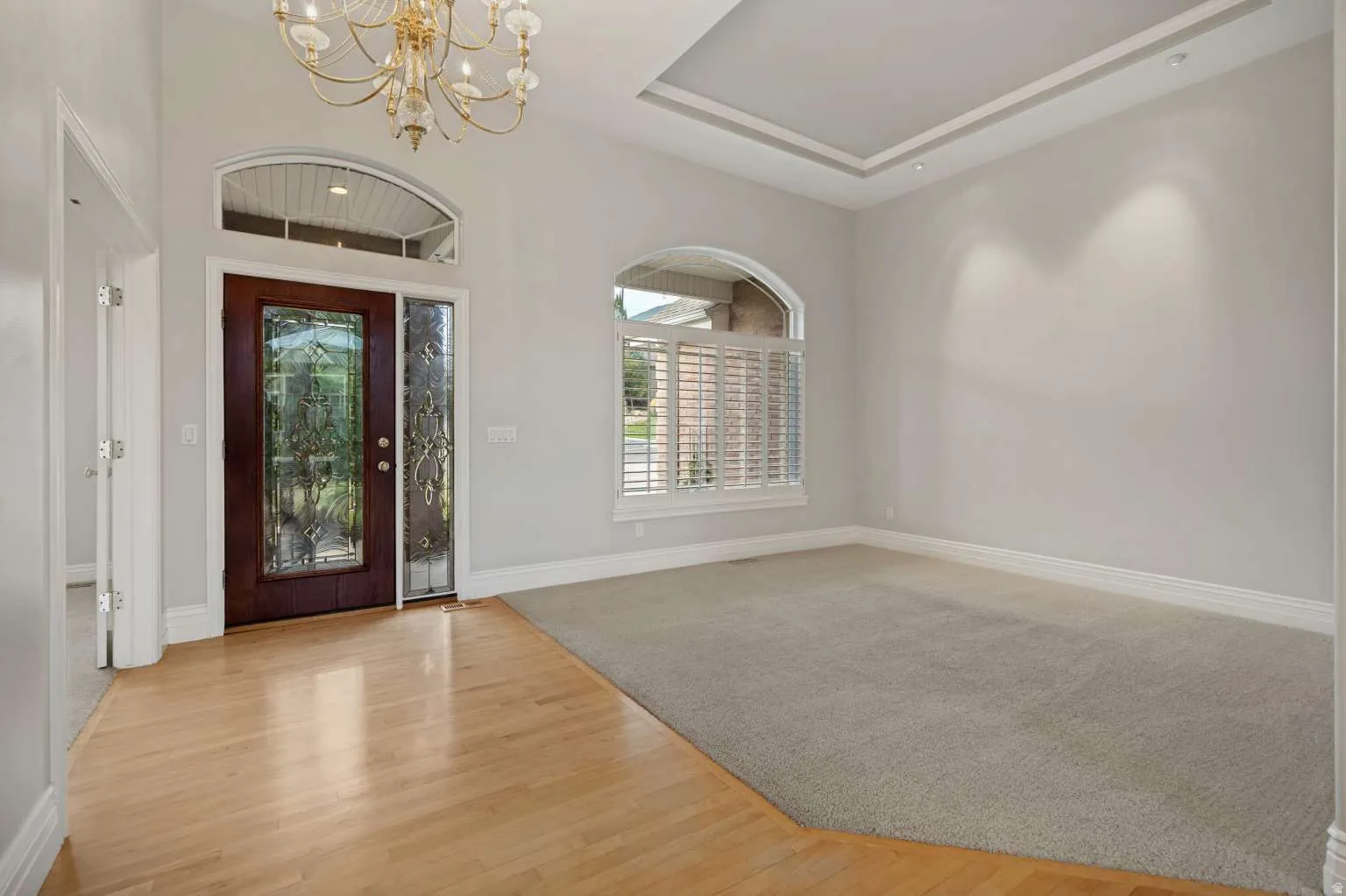 Tray ceiling with recessed lighting, arched windows, wood-finish flooring, leaded glass entry door, and chandelier