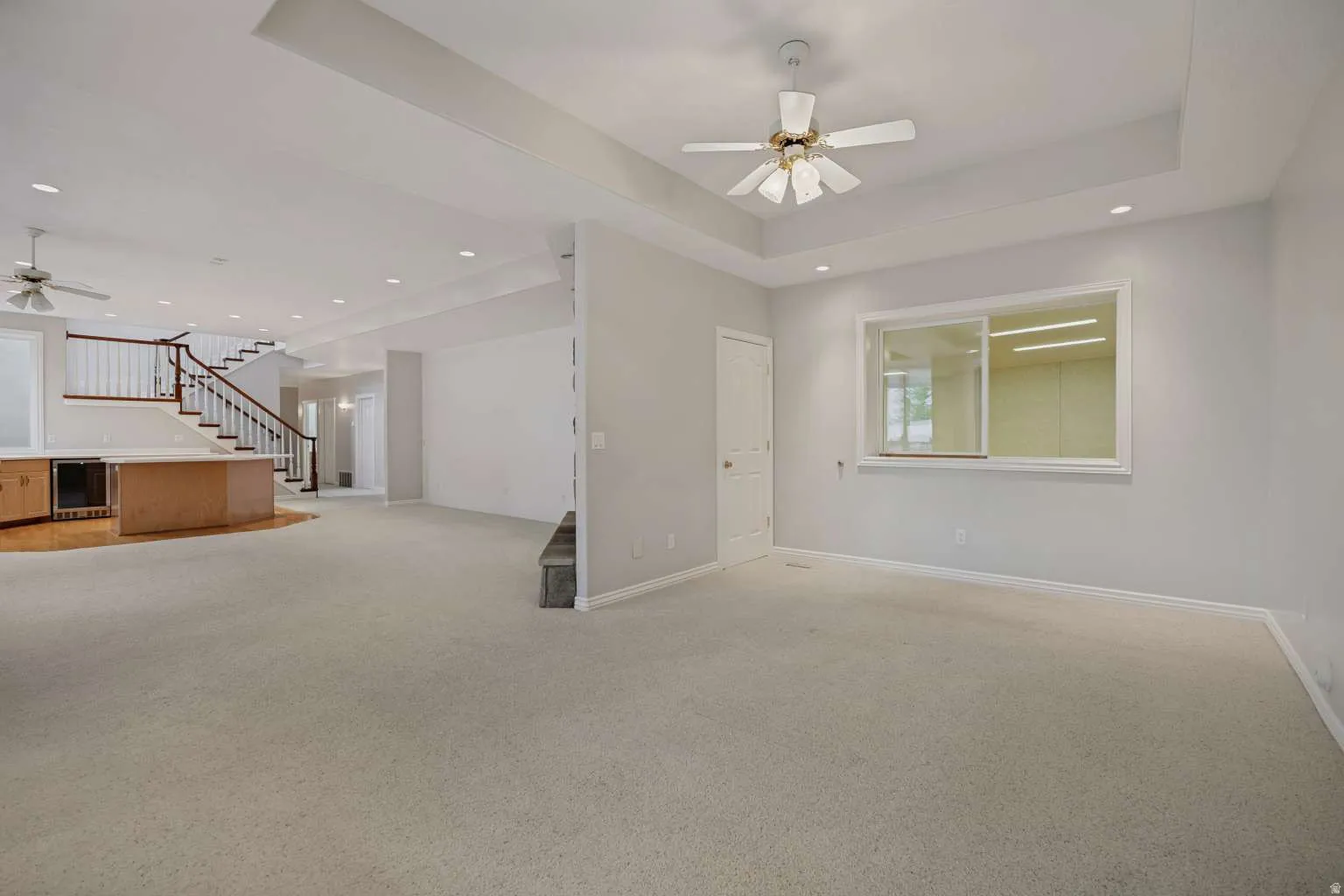 Recessed lighting, ceiling fan, tray ceiling, built-in cabinetry with integrated beverage refrigerator, and a wood-finish staircase with white risers and dark wood handrail